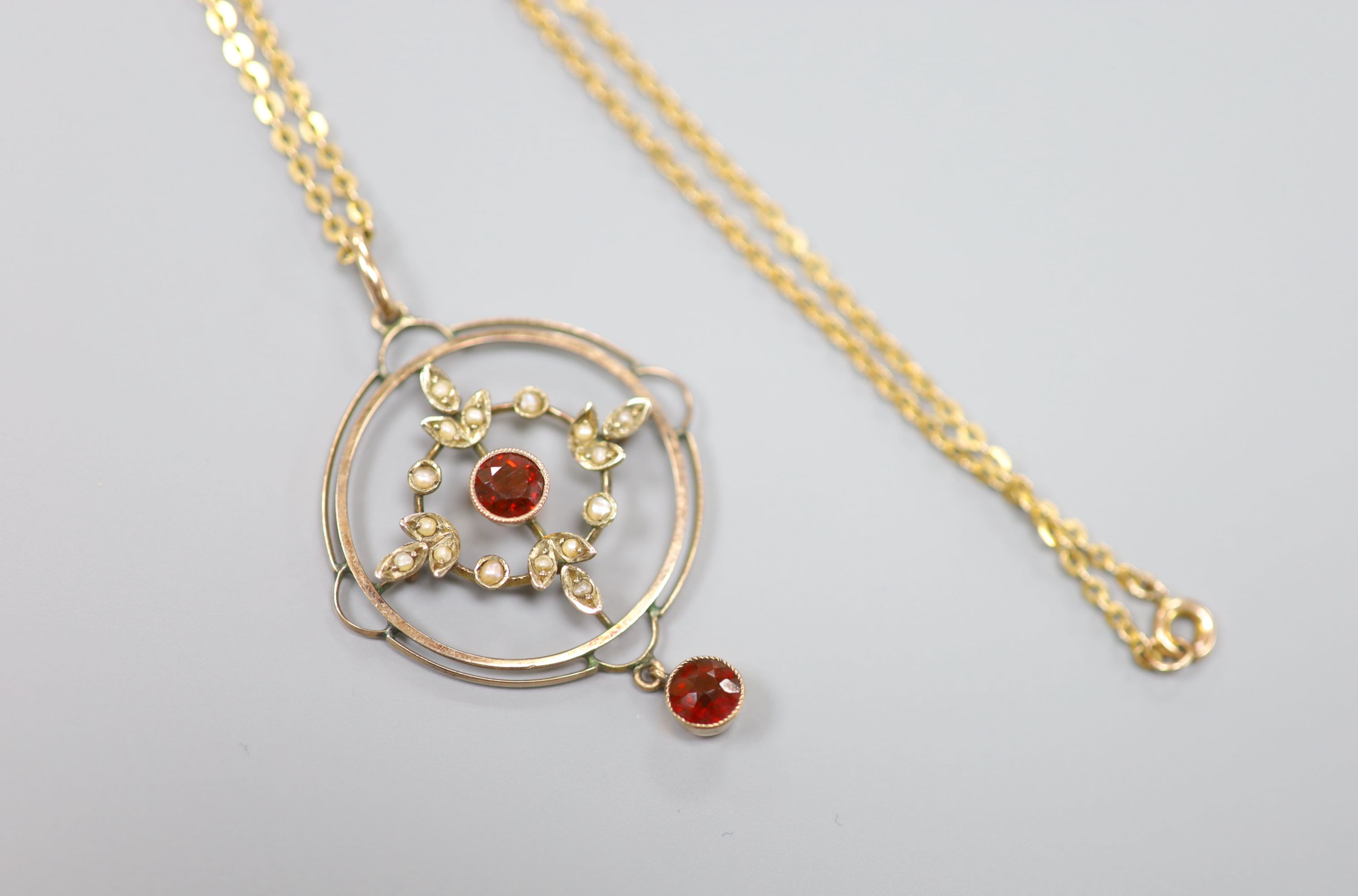 A 9ct, garnet and seed pearl set openwork circular drop pendant, 35mm, on a 9ct chain, 42cm, gross weight 4.9 grams.